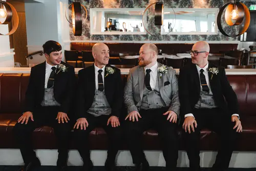 Wedding morning groomsmen in suits relaxing on lounge seating at Redcastle Hotel, Moville, lit by soft window light