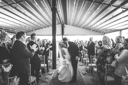 Bride and groom share an aisle kiss during their ceremony recessional at Rossharbour Resort, Lough Erne, as guests applaud