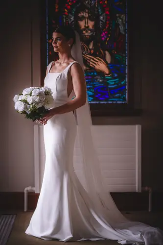 Bride holding a white bouquet in soft window light beside stained glass at Rossharbour Resort, County Fermanagh