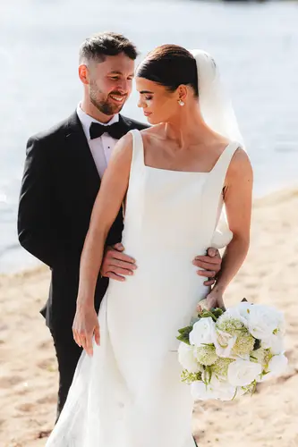 Newlyweds in black tie by the water at Rossharbour Resort, Lough Erne, with bouquet and veil in bright daylight