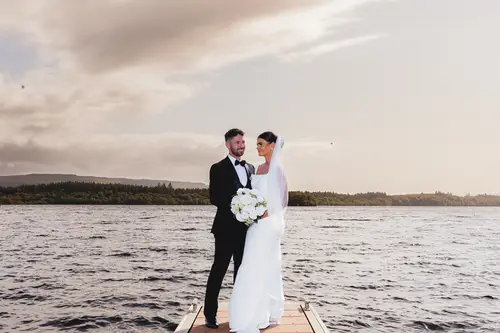 Bride and groom on the dock at Rossharbour Resort, Lough Erne, in soft golden hour light with a wedding bouquet