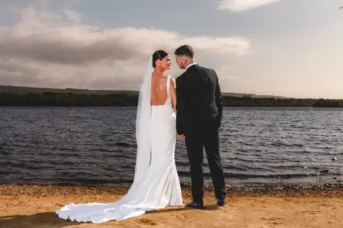 Newlyweds holding hands for lakeside portraits at Rossharbour Resort, Lough Erne, under a soft cloudy sky