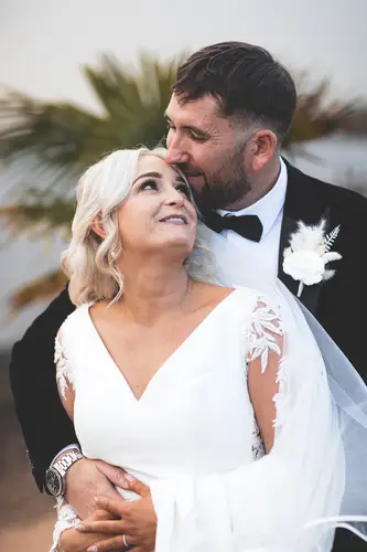 Bride and groom sharing a quiet kiss at Rossharbour Resort, with a bridal veil, black tuxedo and soft palm backdrop