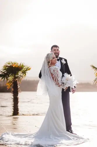 Bride and groom by the waterfront at Rossharbour Resort, Lough Erne, with palm trees and soft backlight