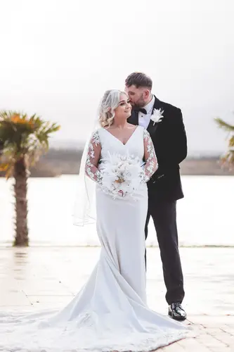 Newlyweds in bright light by the waterfront and palm trees at Rossharbour Resort, Lough Erne