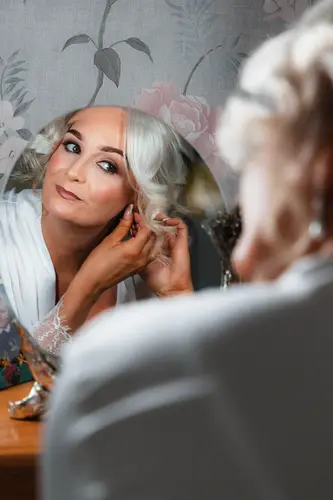 Bride putting on earrings in a mirror during calm wedding morning preparations at Rossharbour Resort, Lough Erne