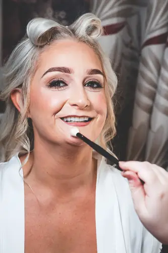 Bride smiling as lipstick is applied during wedding morning prep at Rossharbour Resort, Lough Erne