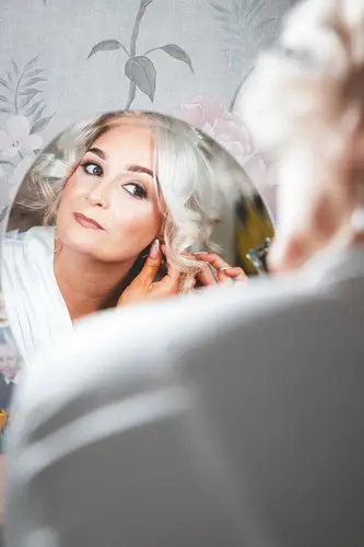 Bride reflected in a mirror putting on earrings during wedding morning prep at Rossharbour resort, Lough Erne
