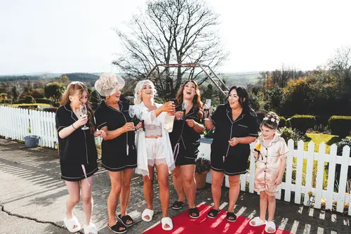 Bride, bridesmaids and flower girl in robes celebrating a champagne pop at Rossharbour Resort, Lough Erne