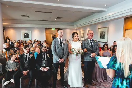 Bride walking down the aisle with her father during an indoor ceremony at Stormont in Belfast