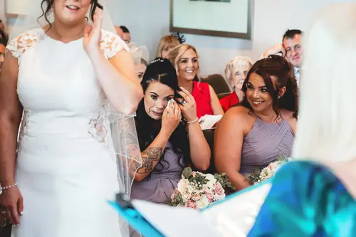 Bride with bridesmaids during an emotional indoor ceremony at Stormont in Belfast, with guests looking on in natural light.