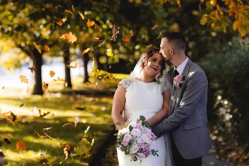 Bride and groom among autumn leaves during couple portraits at Stormont in Belfast, with golden light, bouquet and veil.