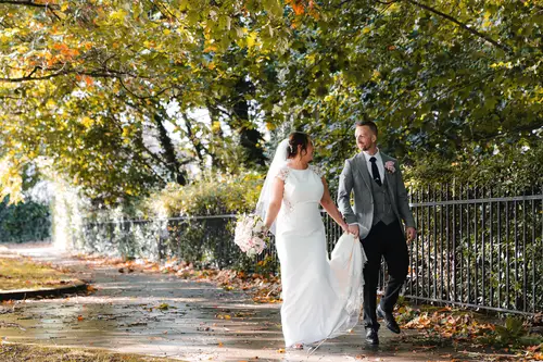 Bride and groom walking along a tree-lined path at Stormont in Belfast during their autumn couple portraits