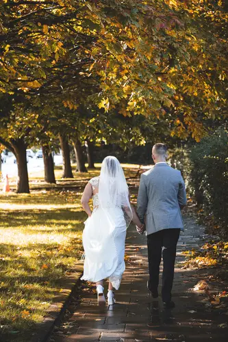 Bride and groom walking along a tree-lined path at Stormont in Belfast, with autumn leaves and soft golden light.