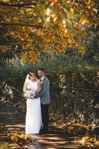 Bride and groom walking through autumn leaves on a garden path at Stormont, Belfast, in warm golden light