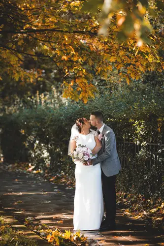 Bride and groom share a kiss on a tree-lined path at Stormont, Belfast, with autumn foliage and soft golden light