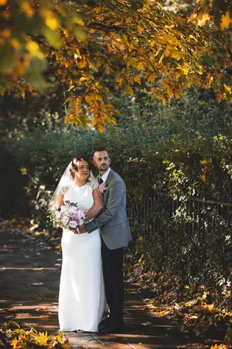 Bride and groom walking on a tree-lined path at Stormont, Belfast, with autumn foliage and dappled natural light