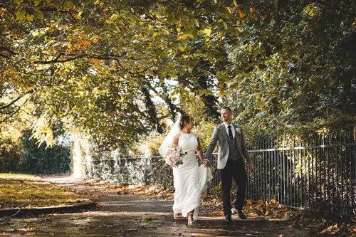 Bride and groom walking together on a tree-lined path at Stormont, Belfast, with autumn leaves and warm natural light
