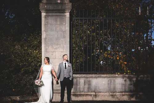 Bride and groom holding hands by the stone gate at Stormont in Belfast with soft dramatic light