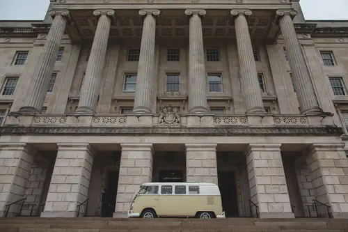 Vintage campervan wedding car outside Stormont in Belfast, framed by grand columns and soft overcast light.
