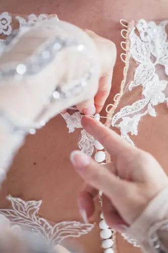 Close-up of hands buttoning a lace wedding dress during bridal prep at Stormont in Belfast