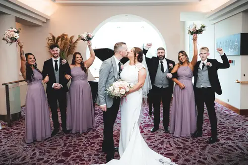 Bride and groom kiss beside their bridal party at Stormont in Belfast, with bouquets and soft window light indoors