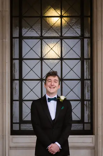 Groom in a black tuxedo and bow tie by a window during wedding morning preparations at Stormont, Belfast.