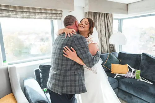 Bride shares a joyful family hug during getting ready at Stormont in Belfast, captured in soft natural light.