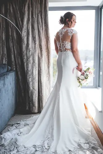 Bride in a lace gown holding her bouquet by the window during wedding preparations at Stormont in Belfast