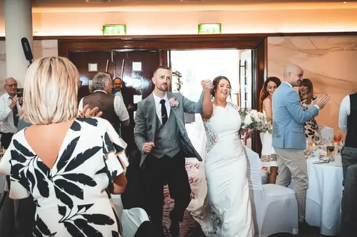 Bride and groom entering their Stormont reception in Belfast to applause from guests under warm indoor light