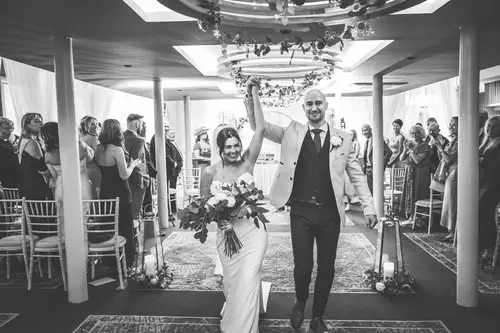 Black and white ceremony aisle exit at Ten Square Belfast, with newlyweds smiling as guests applaud.