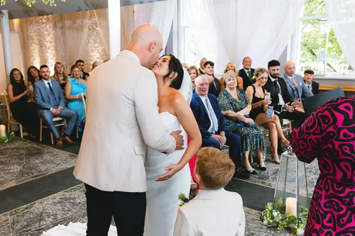 Couple sharing their first kiss during an indoor ceremony at Ten Square in Belfast, with guests looking on.