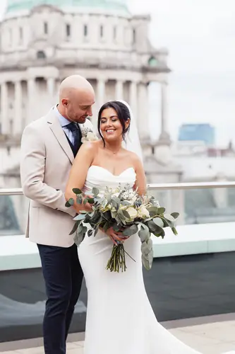 Newlyweds on the rooftop at Ten Square Belfast, with bouquet and soft daylight over the city backdrop