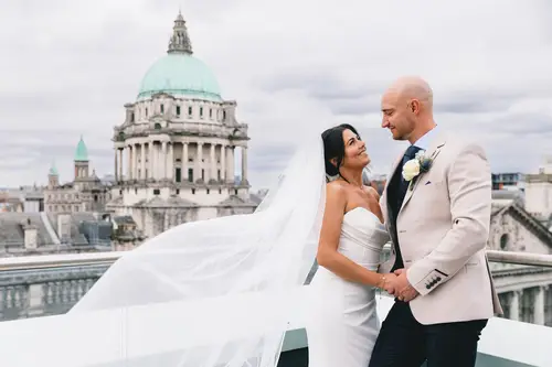 Bride and groom holding hands on the Ten Square rooftop with Belfast cityscape behind them in soft overcast light