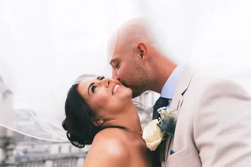 Bride and groom sharing a soft kiss under the veil at Ten Square, Belfast, with wedding flowers close by