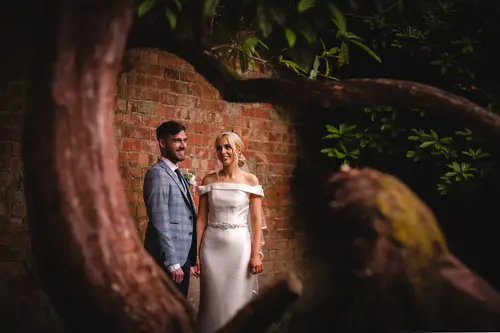 Bride and groom portrait outdoors by a brick wall near Ten Square in Belfast, framed by trees in soft natural light.