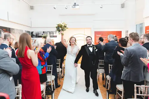 Newlyweds walk back down the aisle at Ulster Museum in Belfast as guests applaud during their ceremony recessional.