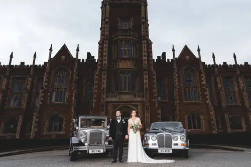 Bride and groom portrait beside vintage wedding cars outside Ulster Museum in Belfast under soft overcast light