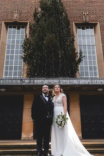 Bride and groom portrait outside Ulster Museum in Belfast, with a bouquet, brick facade and Christmas tree in natural light
