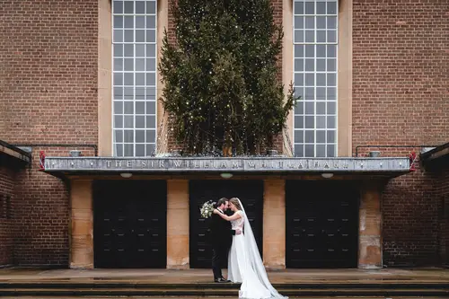Bride and groom sharing a kiss by the brick entrance of Ulster Museum in Belfast