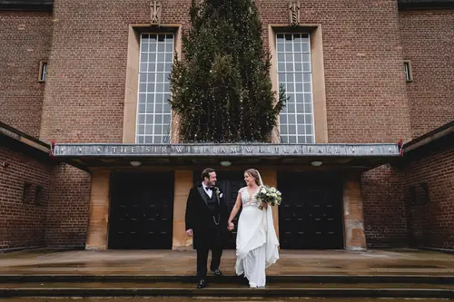 Bride and groom walking together outside Ulster Museum in Belfast, with a brick backdrop and soft overcast light