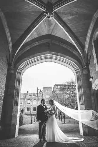 Black and white couple portrait under an archway at Ulster Museum Belfast, with the bride’s veil flowing in natural light.