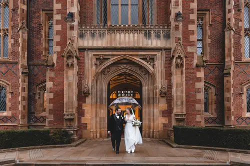 Bride and groom under an umbrella outside Ulster Museum in Belfast on a rainy wedding day