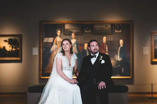 Bride and groom seated in a moody Ulster Museum gallery in Belfast, with artwork behind them for a relaxed wedding portrait