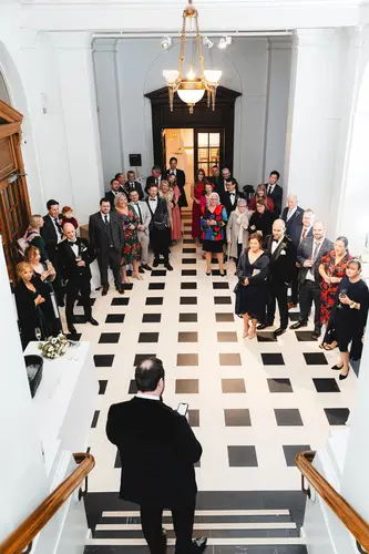 Wedding guests listen to a reception speech under chandelier light at Ulster Museum in Belfast