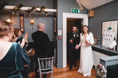Newlyweds enter their Ulster Museum reception in Belfast as guests clap under warm indoor light