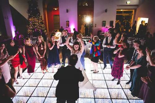 Couple and wedding guests dancing under bright lights at an Ulster Museum reception in Belfast